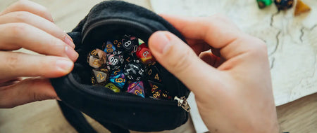 Hands holding open a black zippered plush dice bag full of polyhedral dice, zipper pull visible on the side