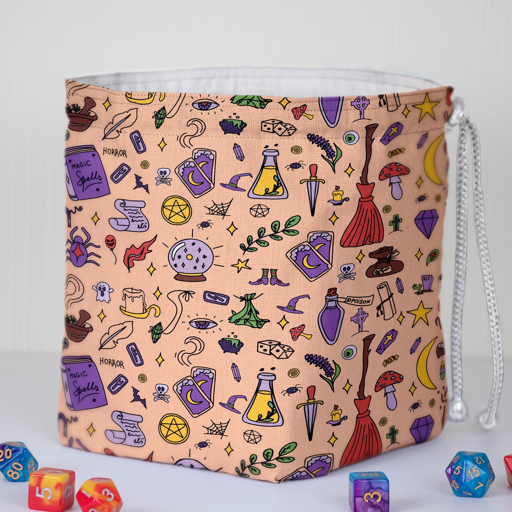 A dice bag that feels authentically witchy — peach spellcraft doodles with crystal balls, brooms and potions, holds 300+ dice.