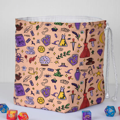 A dice bag that feels authentically witchy — peach spellcraft doodles with crystal balls, brooms and potions, holds 300+ dice.