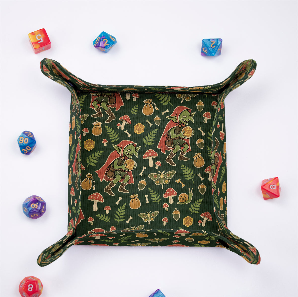 Forest Goblin dice tray from above, moss green fabric with red-hooded goblins, fly agaric mushrooms, ferns and moths, colorful dice around it