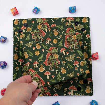 Forest Goblin dice tray folded flat, hand lifting the removable hard insert covered in the same mushroom goblin print