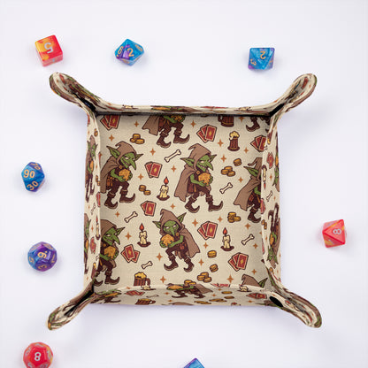 Tavern Goblin dice tray from above, cream fabric printed with hooded goblins, playing cards, ale mugs and candles, with colorful dice around it