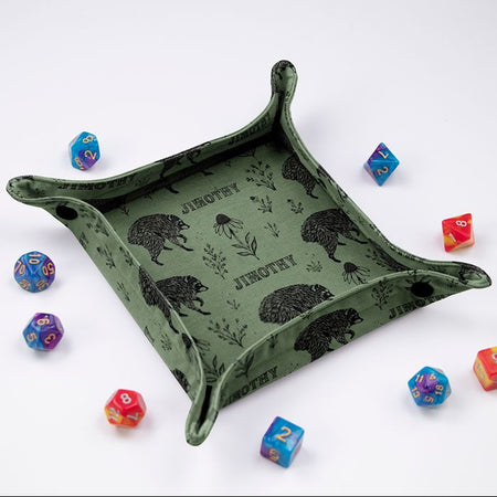 Jimothy sage botanical dice tray at an angle, black raccoons and wildflowers on sage green fabric, colorful dice around it