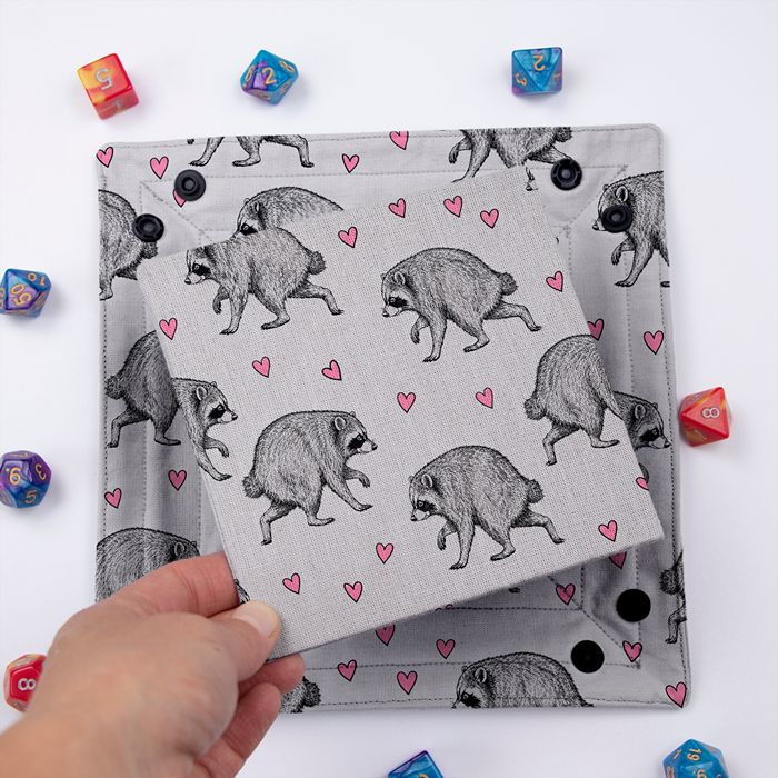 Jimothy dice tray folded flat, hand lifting the removable hard insert covered in the same raccoon print
