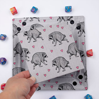 Jimothy dice tray folded flat, hand lifting the removable hard insert covered in the same raccoon print