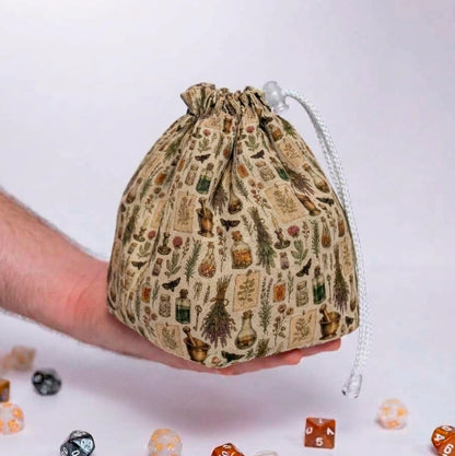 Apothecary's Shelf dice bag held in a hand, herbalist print with potion bottles, mortar and pestle, dried herbs and moths