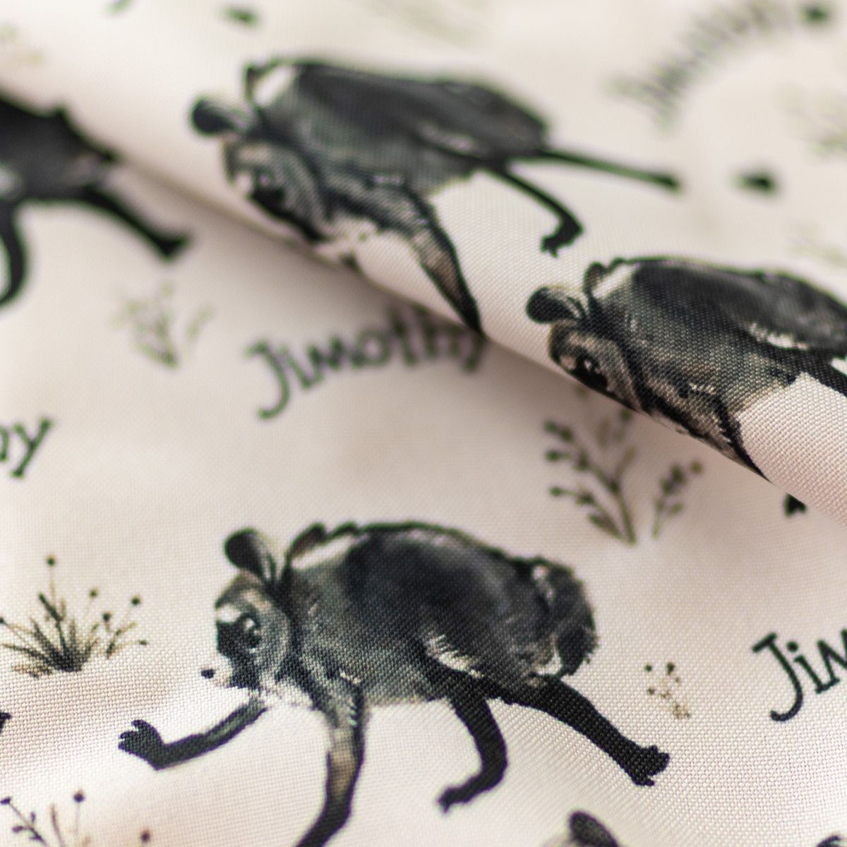 Close-up of GameFancy Jimothy signature print fabric, raccoons and his name on cream, used for dice bags