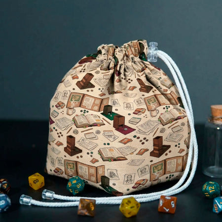 Dungeon Master's Desk dice bag standing on a dark table, beige fabric printed with game books, dice towers and table maps