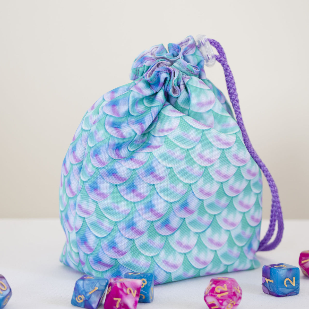 Custom printed small dice bag example: teal and purple mermaid scale pattern, drawstring closed, DnD dice beside