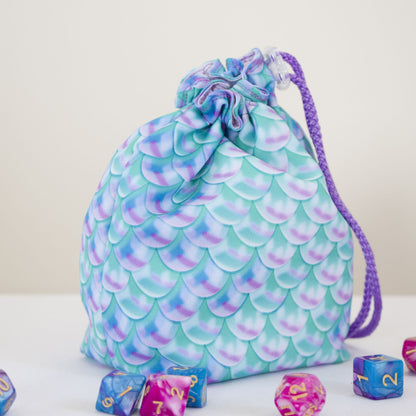 Custom printed small dice bag example: teal and purple mermaid scale pattern, drawstring closed, DnD dice beside