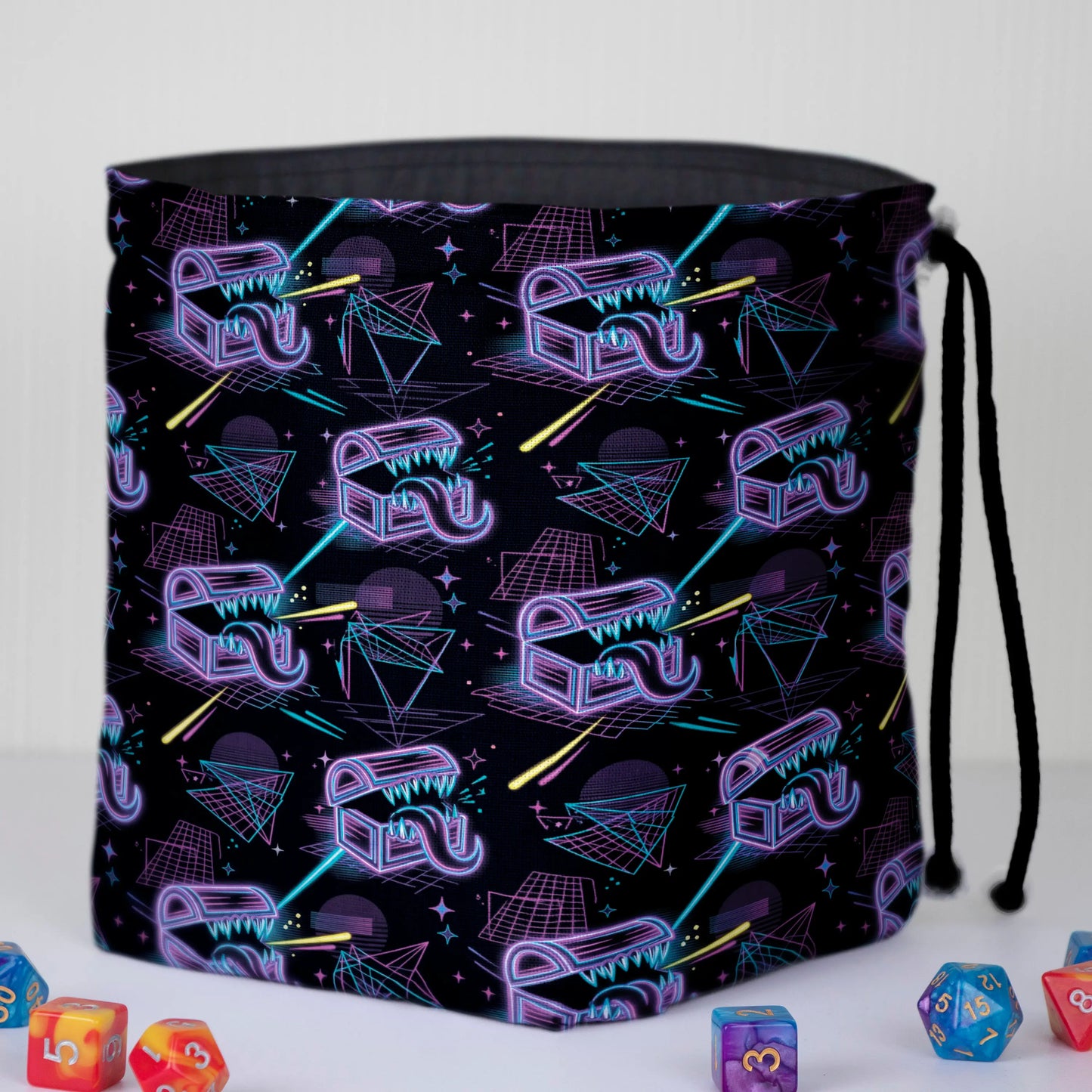 Neon mimic dice bag held in hand — purple and cyan wireframe mimic print, drawstring closure