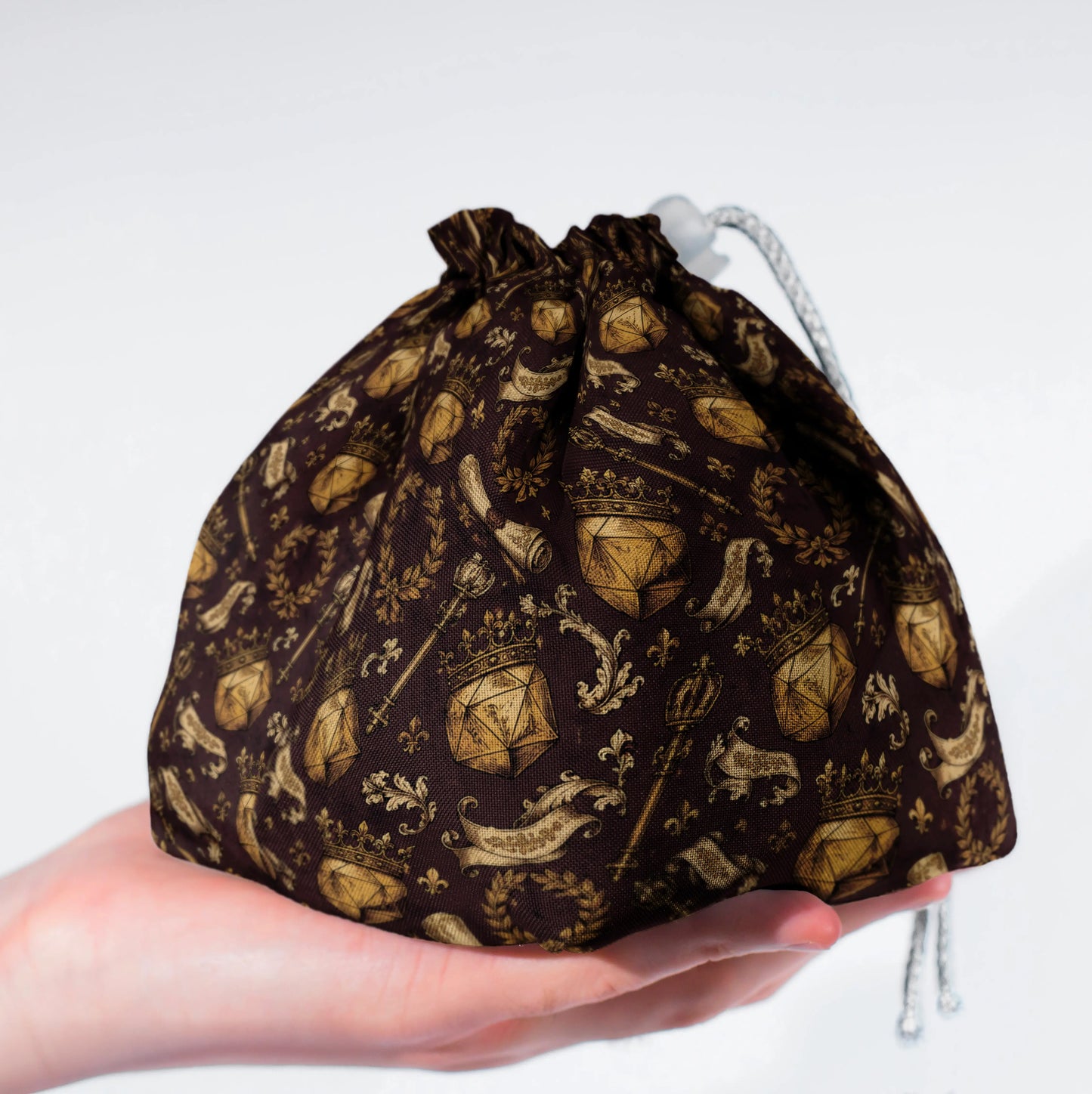 Close-up of the heraldic print — gold D20 crests, crowns and laurels on brown gabardine.