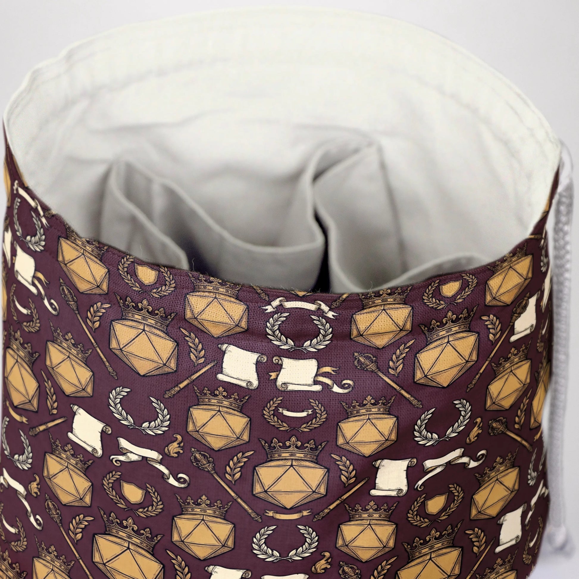 Close-up of the DM crown print — gold D20 shields, crowns and laurels on burgundy gabardine.