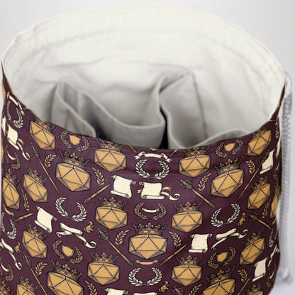 Close-up of the DM crown print — gold D20 shields, crowns and laurels on burgundy gabardine.