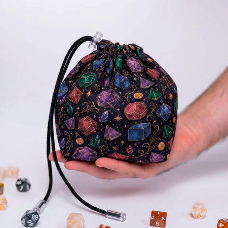 Celestial Crystal dice bag with pockets held in a hand, black fabric with watercolor gemstone dice and gold stars