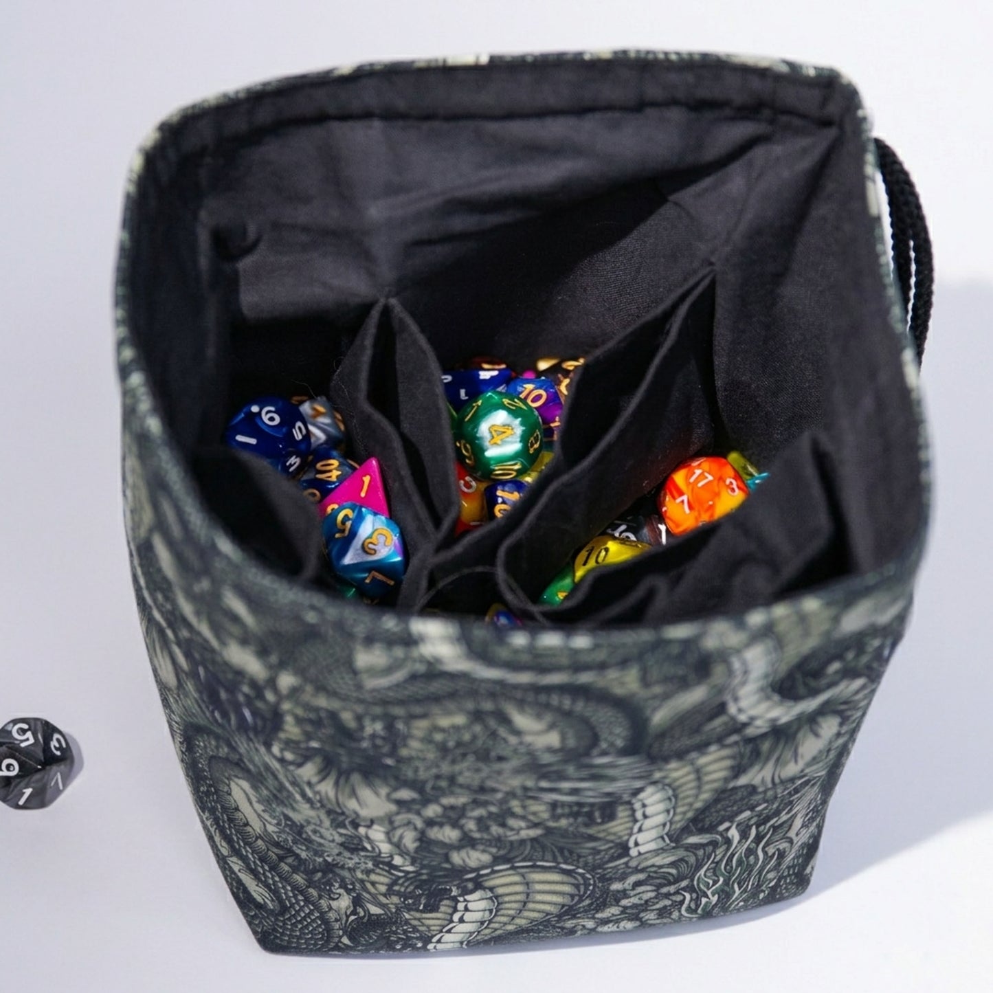 Handmade black-and-white dragon dice bag open to show 6 pockets and colorful dice — 300+ capacity.