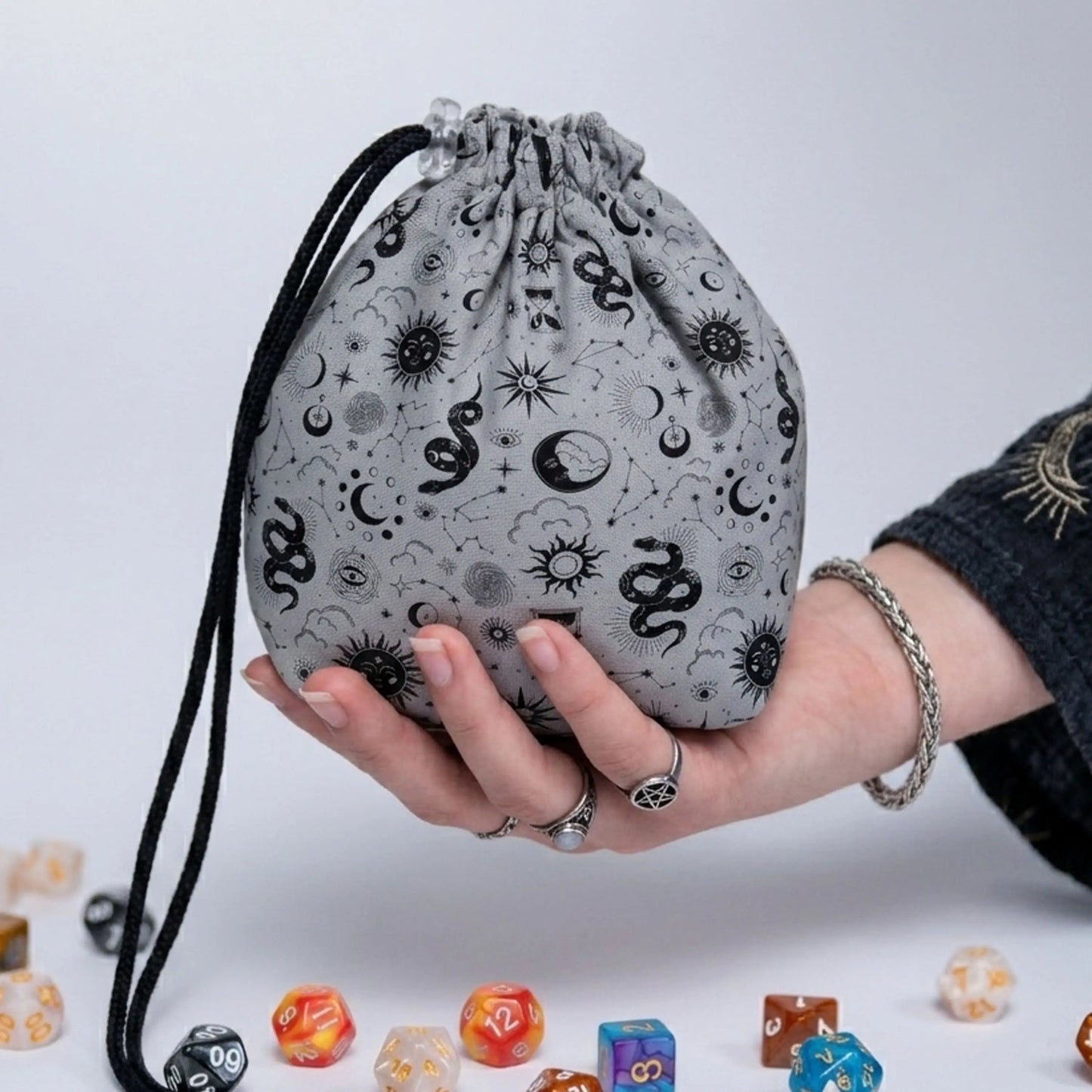A dice bag that matches your witchy aesthetic — black serpents, suns and moons on soft gray, holds 300+ dice.