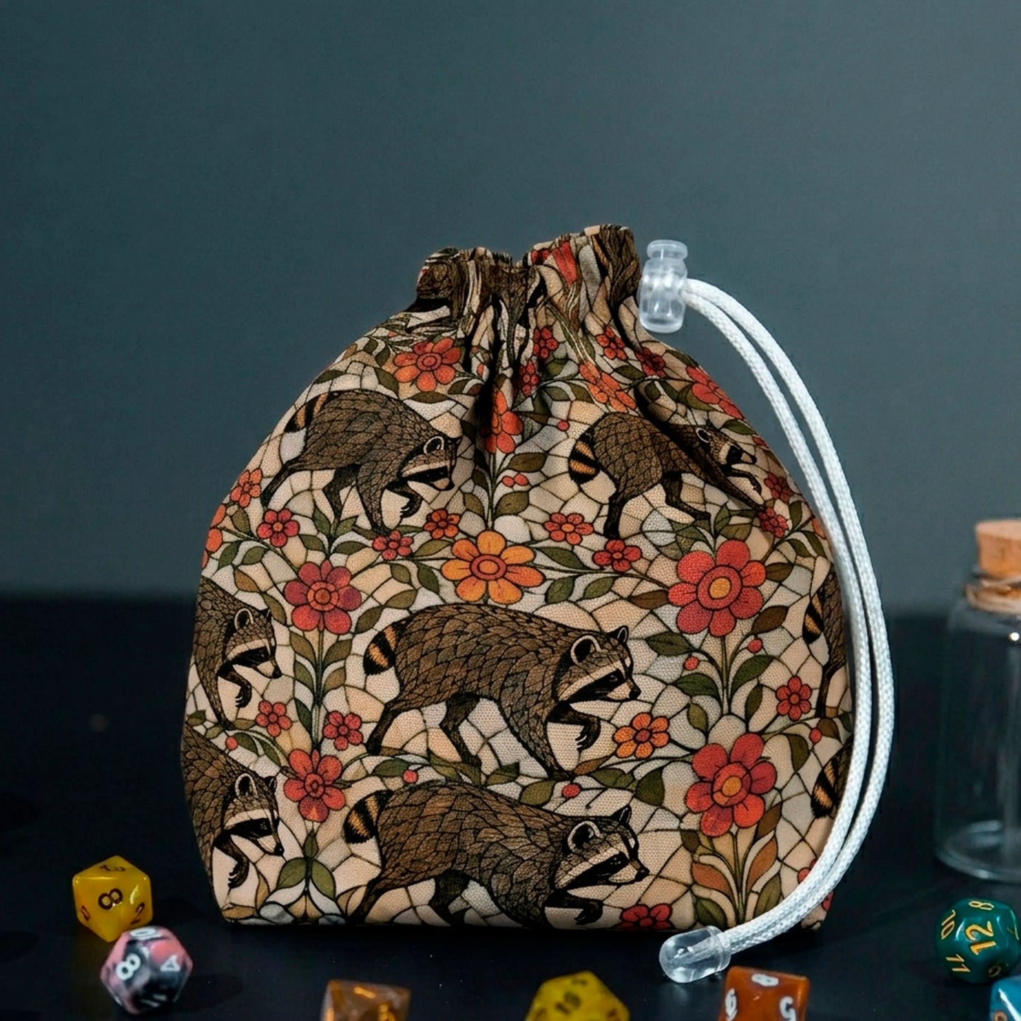 Jimothy raccoon dice bag in warm stained glass garden print with cream, red and orange flowers, with DnD dice
