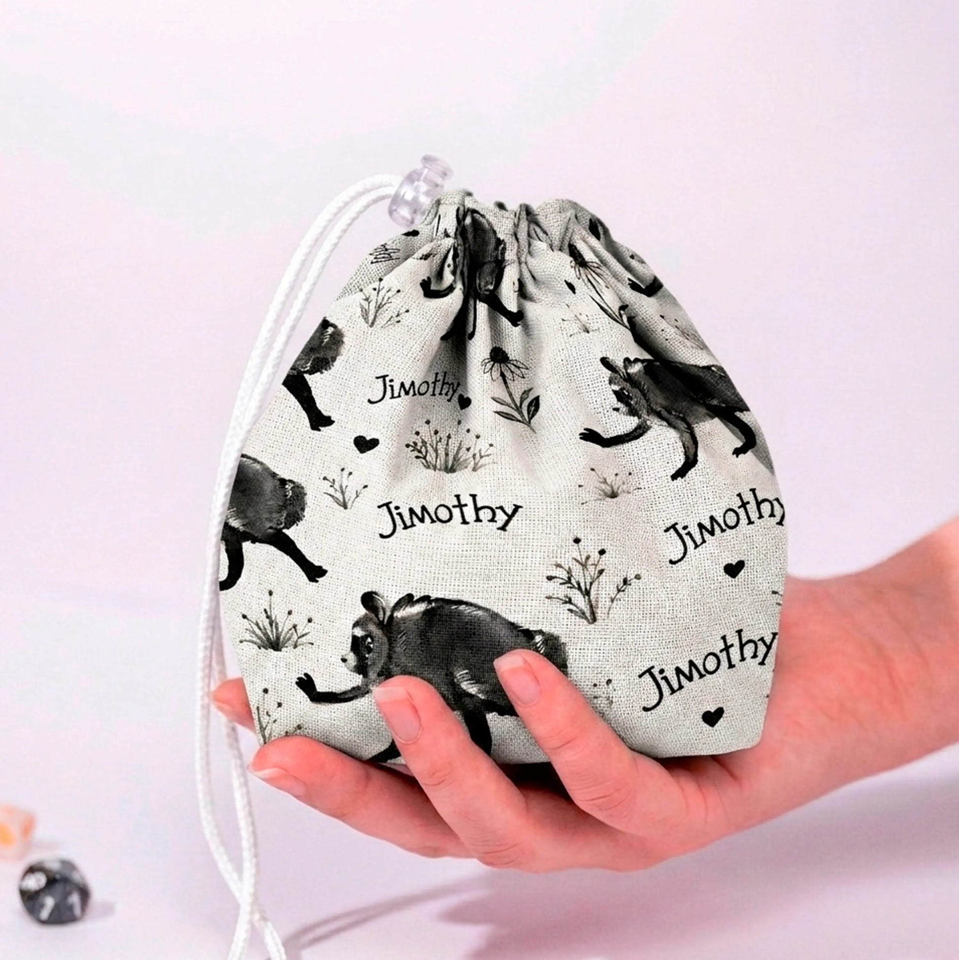 Jimothy raccoon dice bag in cream ink sketch print with handwritten Jimothy script and hearts, held in a hand