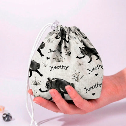 Jimothy raccoon dice bag in cream ink sketch print with handwritten Jimothy script and hearts, held in a hand