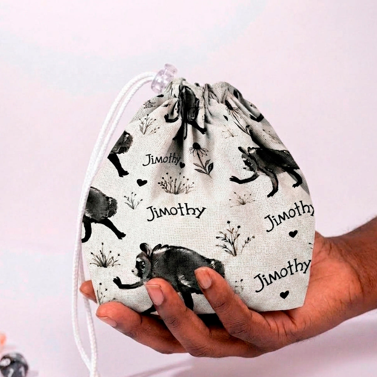 Jimothy raccoon dice bag in cream ink sketch print with handwritten Jimothy script and hearts, held in a hand