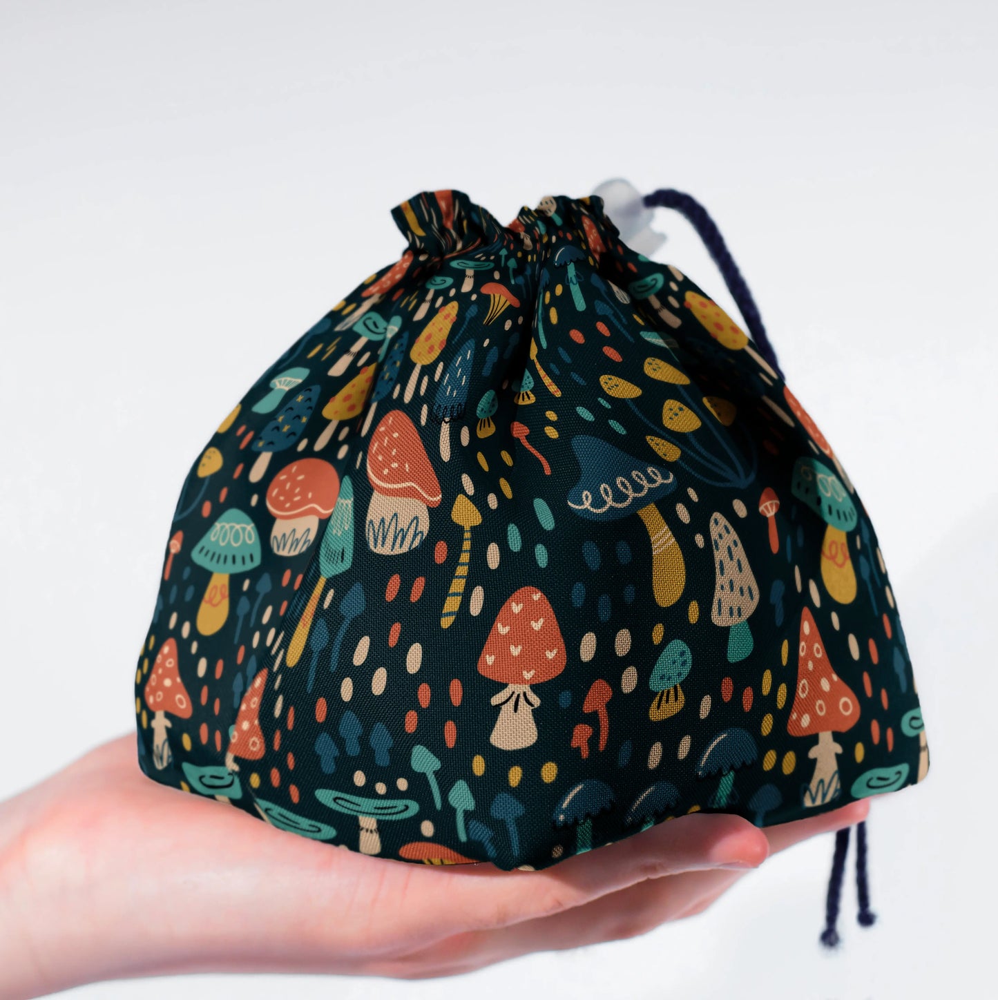 A cottagecore dice bag with whimsical folk mushrooms on deep teal, holds 300+ dice.