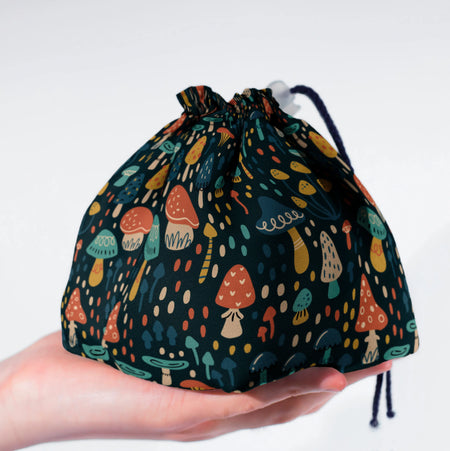 A cottagecore dice bag with whimsical folk mushrooms on deep teal, holds 300+ dice.