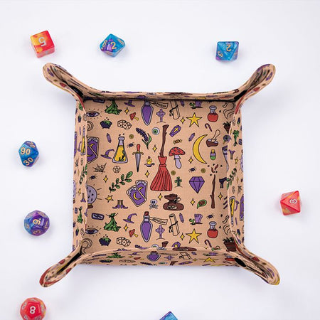 Witchy dice tray from above, peach fabric with brooms, potions, moons and crystal balls, colorful dice around it