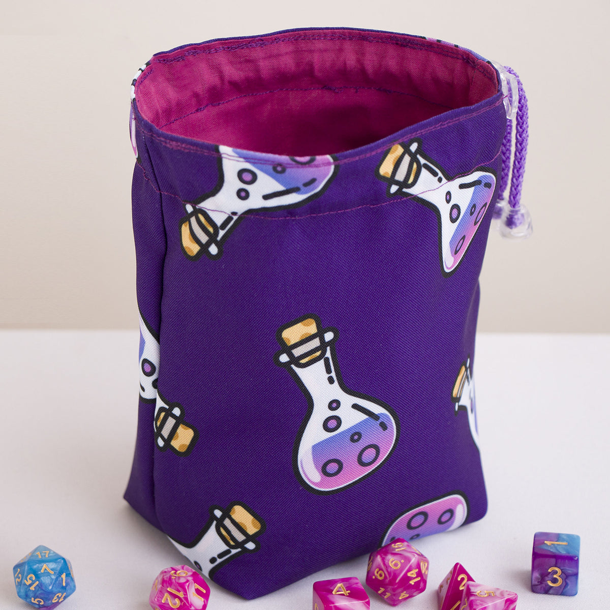 Purple potion print custom dice bag open, pink cotton lining, DnD dice sets beside