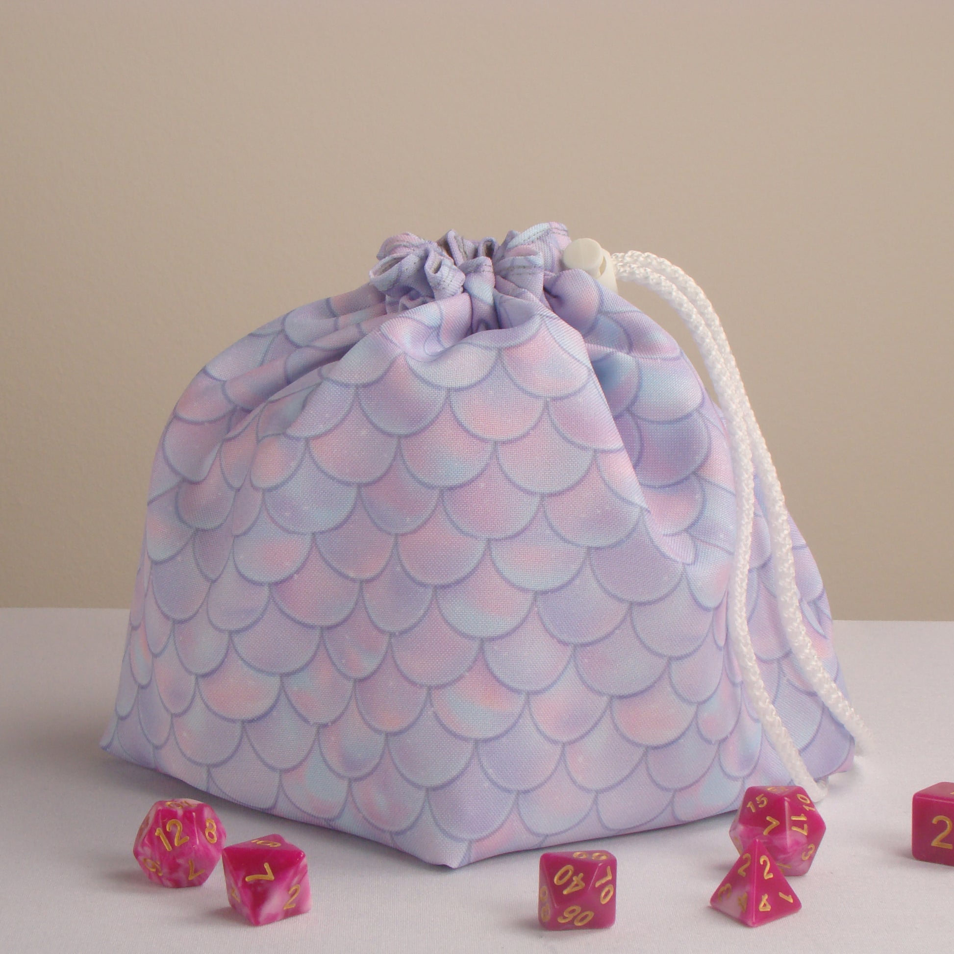 Handmade pastel pink-and-lavender dragon-scale dice bag holding 300+ dice — gabardine fantasy pouch.