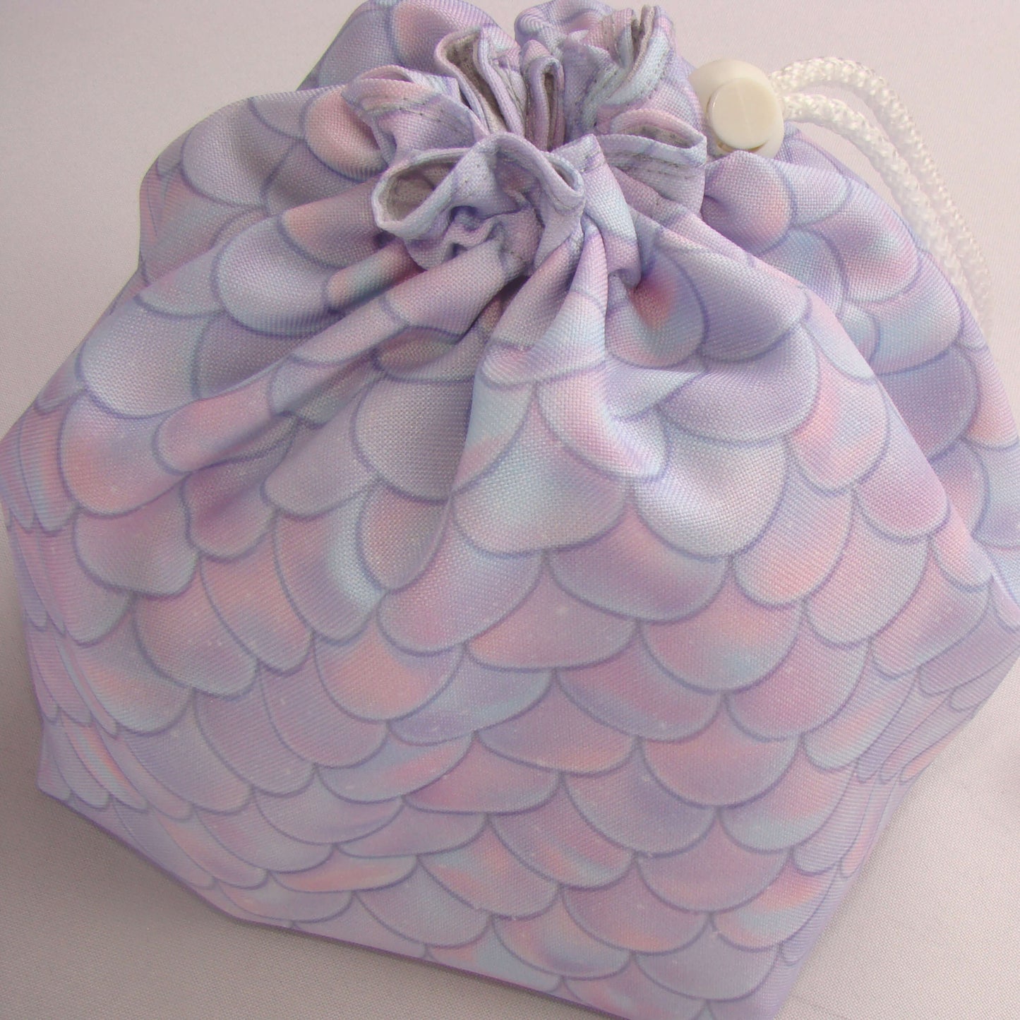 Pastel dragon-scale dice bag shown with dice for scale — soft fantasy DnD organizer.