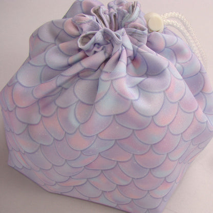 Pastel dragon-scale dice bag shown with dice for scale — soft fantasy DnD organizer.
