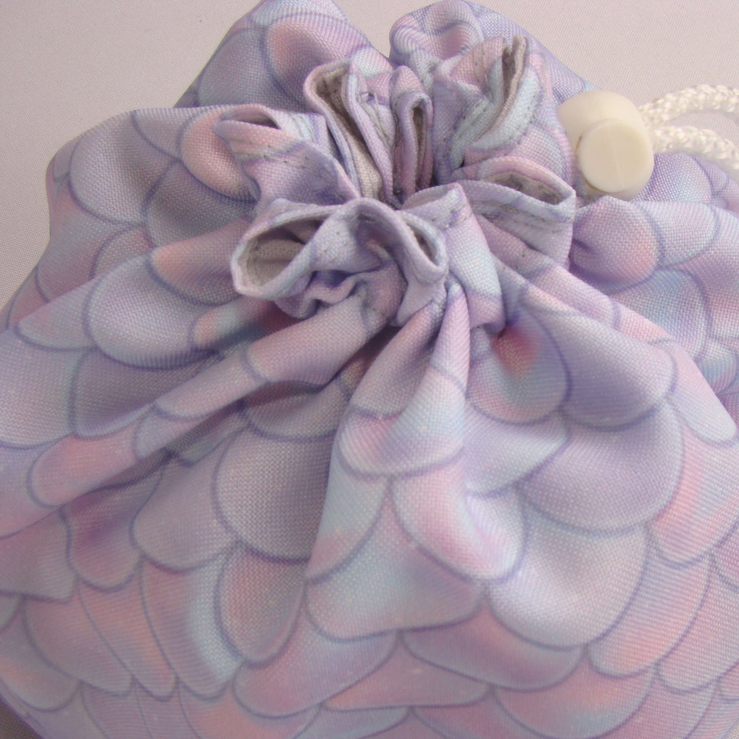 Pastel dragon-scale dice bag with white drawstring drawn closed — handmade fantasy pouch.