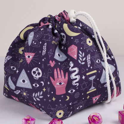 A dice bag that matches your witchy aesthetic — palmistry hand, all-seeing eyes and crystals on deep purple, holds 300+ dice.