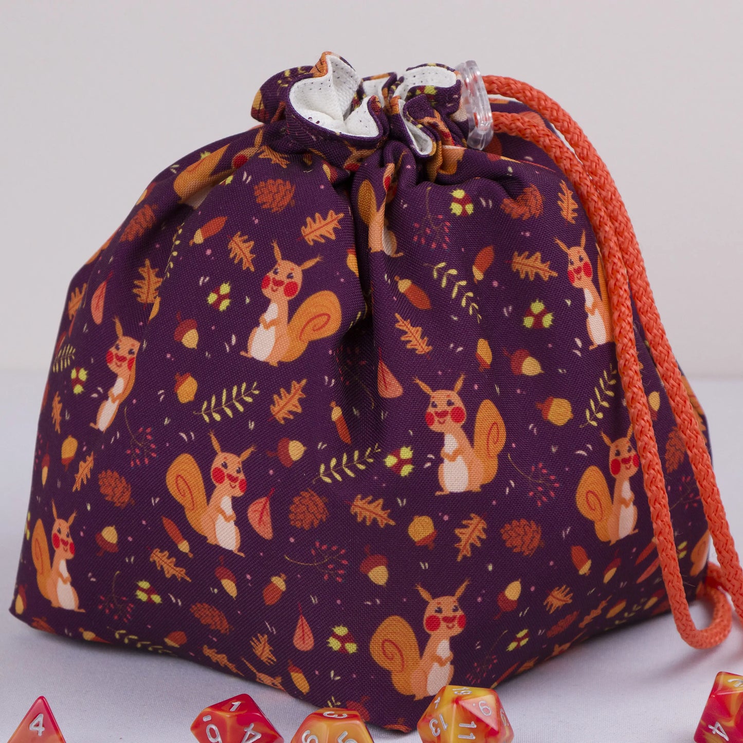 A cottagecore dice bag that fits your vibe — cute squirrels, acorns and autumn leaves on plum, holds 300+ dice.