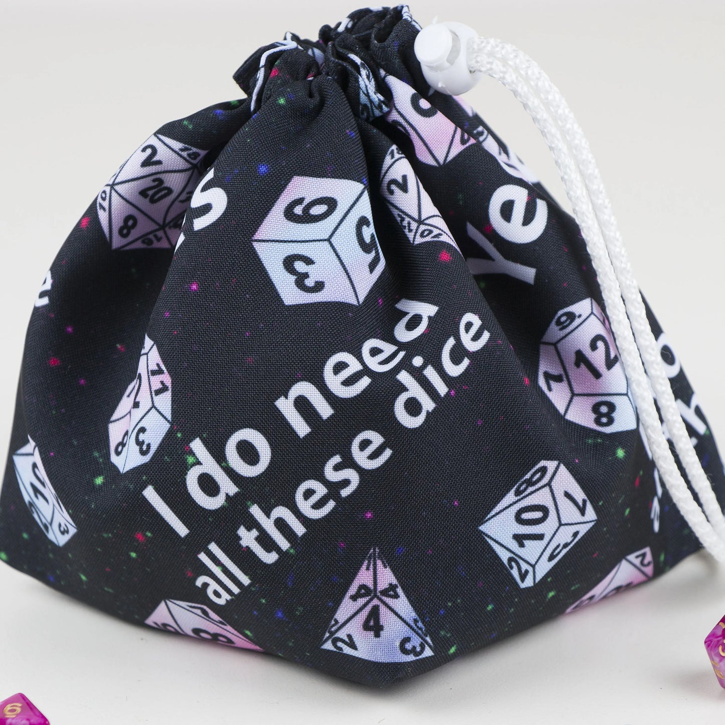 Close-up of the print reading 'Yes I do need all these dice' with pastel polyhedral dice on black gabardine.